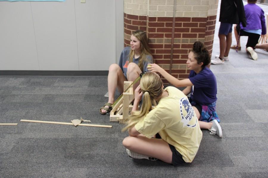 Karl Gscheidle’s physics class tests student made catapults Monday in the main hallway of Coppell High School. Juniors Sarah Houchin, Rachel Kruise and Katie Herklotz sit in the hall to run their trials on the experiment. Photo By Chelsea Banks.

