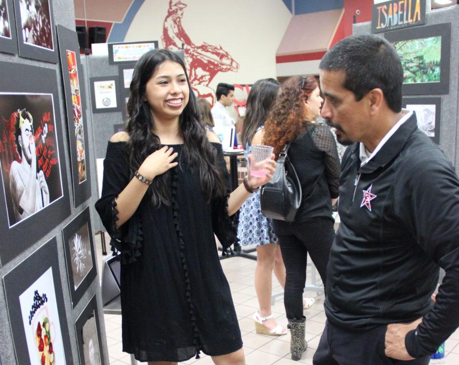 Coppell High School junior Giuliana Vargas presents her artworks to principal Mike Jasso during the AP/IB art showcase on Thursday. Vargas’s chosen concentration was two-dimensional art.