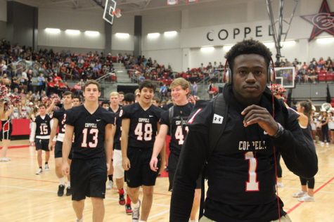 Coppell High School senior running back Tim Heard and the rest of the varsity football team walk into the pep rally through the line of cheerleaders Friday morning at the senior pep rally in the arena. Photo by Hannah Tucker.