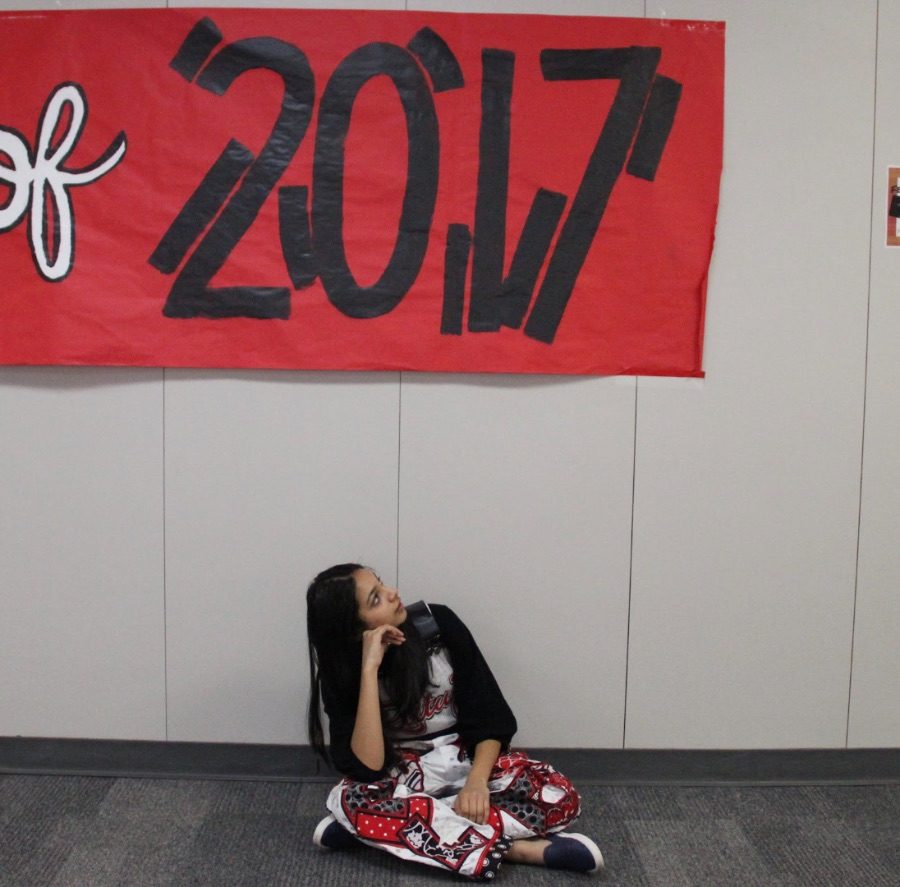 Cutline: Coppell High School senior Rutuja Joshi reflects on her last semester of high school. Posing under the class of 2017 sign, Joshi wears “senior overalls” to participate in the CHS senior year tradition. 

