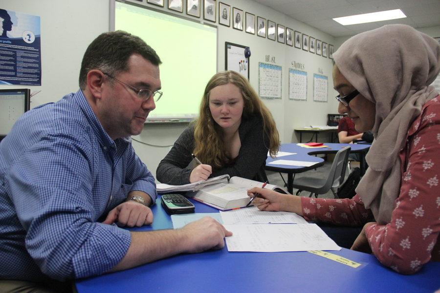 IB Math Studies teacher Ian VanderSchee works with seniors Jess Goode and Maria Khan on their trigonometry homework. VanderSchee teaches using the flipped classroom method, where students learn the material at home through videos and can ask questions and work out problems with him during class.