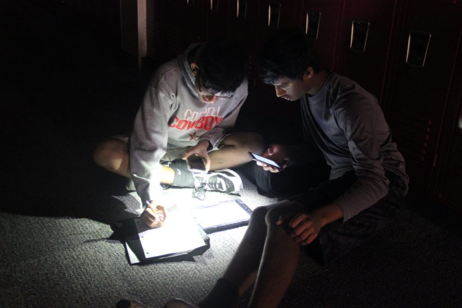 Coppell High School freshmen Nirrangan Akilan and Aditya Putrevu work on classwork in the hallway during the power outage Tuesday morning. Using phone lights, the students were able to continue working during the outage.