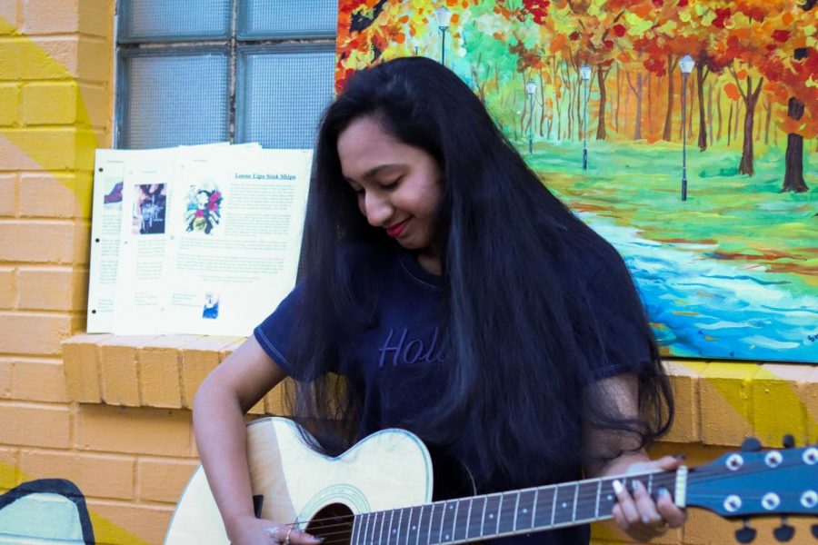 Freshman Shraavya Pydisetti plays her guitar in front of a mural in downtown Carrollton on Jan. 11. Pydisetti is involved in a variety of artistic interests, including writing, guitar, dance and art.