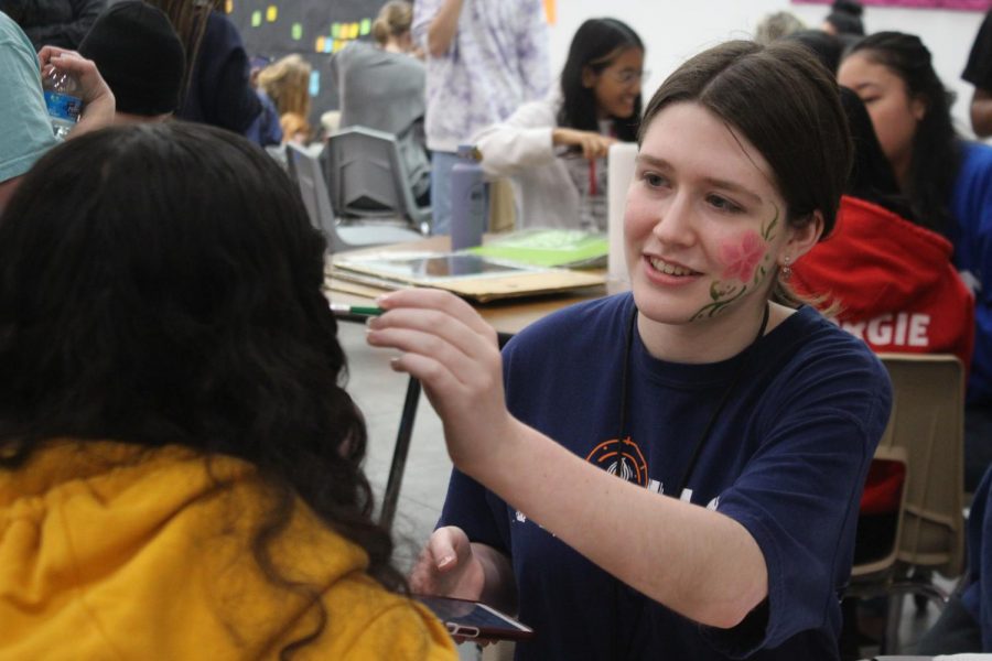 Coppell High School junior Jordan Cohen paints a flower on sophomore Arshi Sharma during A lunch in the Large Commons on Thursday. Students in National Art Honor Society throughout the day orchestrate art activities during all lunches today.