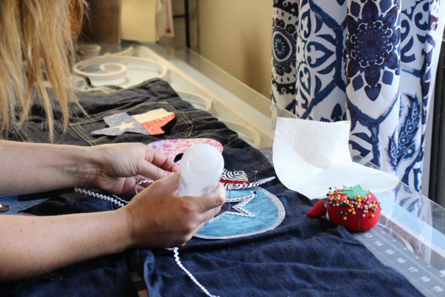 Jewels N Cotton sales and marketing manager Jennifer Ham glues a patch on a pair of senior overalls on Sept. 19. Founder Julie Urbach and Ham are a daughter and mother duo who make senior overalls and other spirit wear for students.
