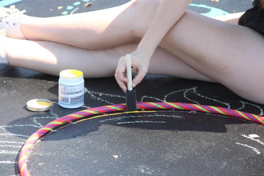 Coppell High School senior Lauren Chamberlain uses a hula hoop to trace a circle for her parking spot design at the CHS parking lot on Saturday. Seniors were able to paint their assigned parking spots from 9 a.m. to 4 p.m.