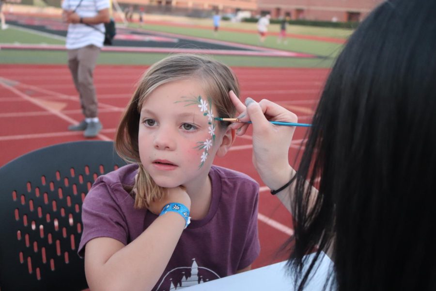 Coppell High School junior Emily Chang paints a vine of flowers on Cottonwood Creek Elementary fourth grader Charlotte Axelson at the face painting station at Buddy Echols Field on Saturday. The CHS Student Council hosted a Monsters, Inc. movie night to raise funds for the Class of 2023 prom. 