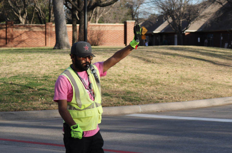 Coppell High School crossing guard Anthony Saldana stops a bus to let students walk across the road at the bus loop after school on Jan. 18. Saldana has worked at CHS for four years and serves as the head of security.