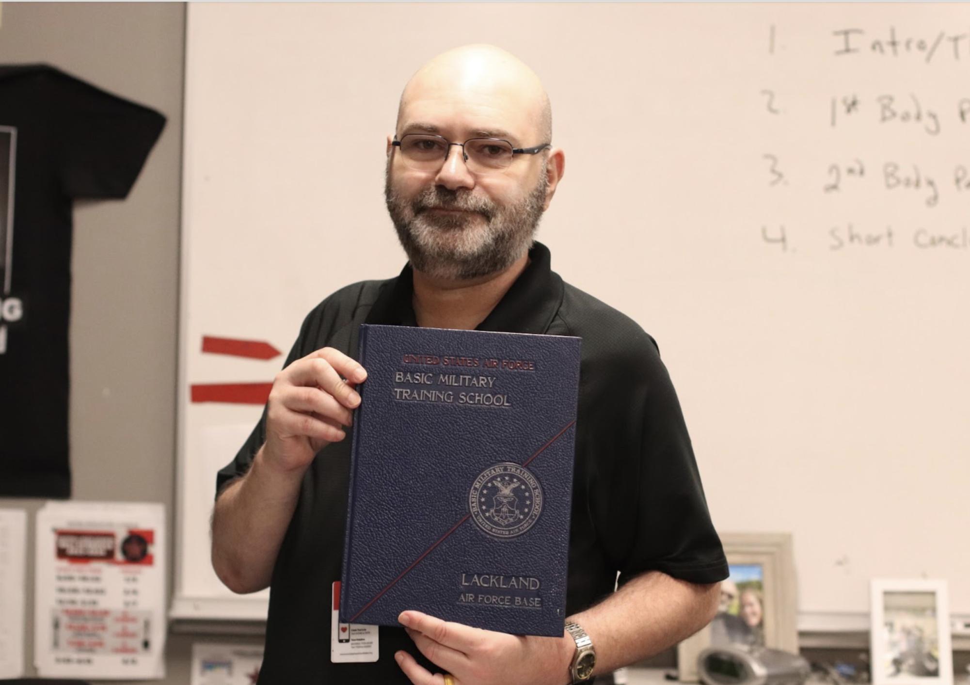 Coppell English II teacher David Poskey holds the yearbook of the United States Air Force Basic Military Training School as a reflection of his life that has led him to where he is now. Poskey has been selected as The Sidekick’s Volume 35 No. 2 Teacher of the Issue.