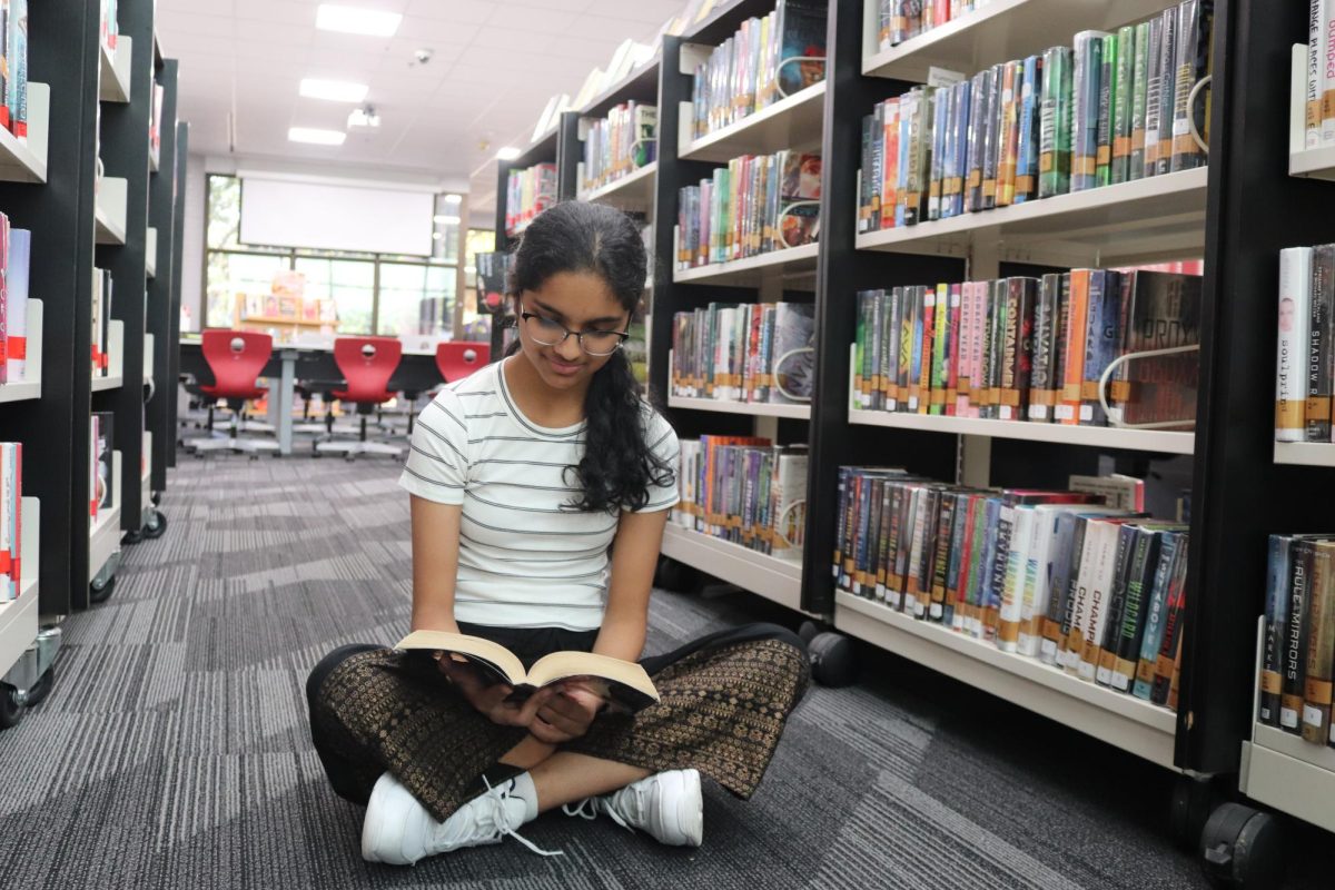 The Sidekick staff designer Nrithya Mahesh reads Cinder by Marissa Meyer in the Coppell High School Library. Mahesh finds solace and comfort in the familiarity of rereading books. Photo by Sukirtha Muthiah