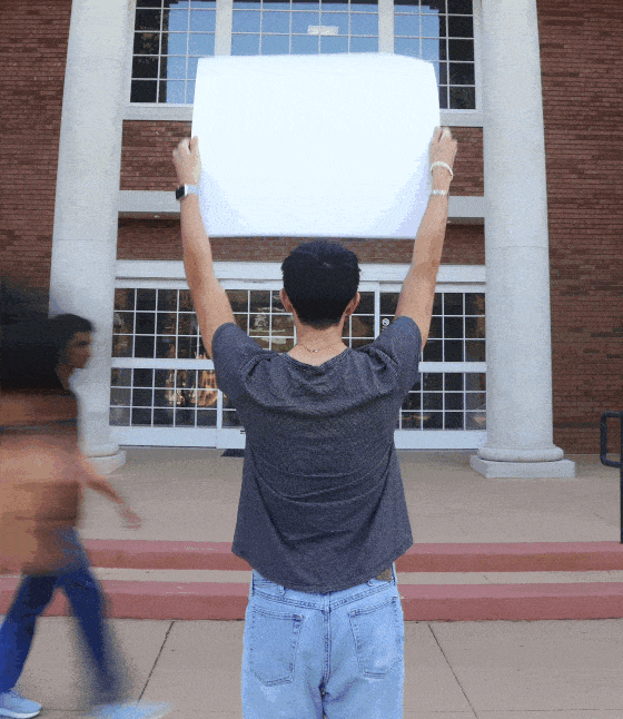 Coppell High School senior Jonas Rogers holds up a sign in front of Coppell City Hall as senior Rebekah Seymour and junior Aryaman Singh walk across. Coppell offers an environment which encourages students to think more openly about political issues. Photo by Wendy Le