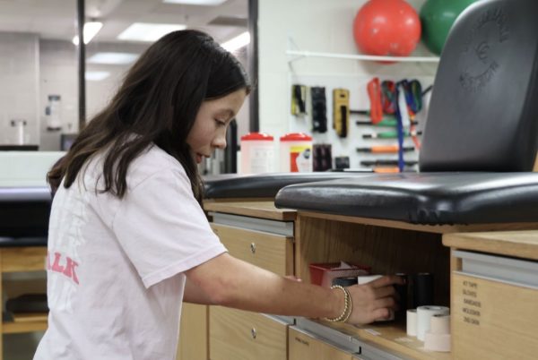 Coppell High School sophomore Adaline Arnold organizes sports medicine supplies in the CHS Field House training room. Arnold has stiff skin syndrome, a rare genetic disorder causing the skin to harden and affects joint movement.