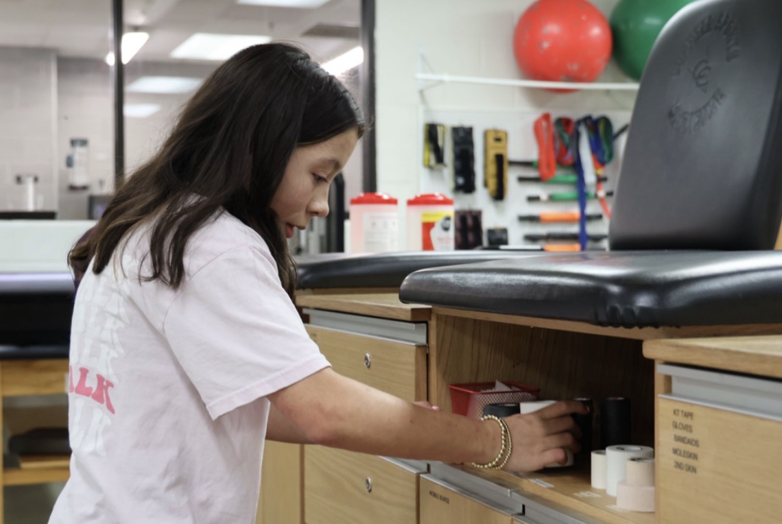 Coppell High School sophomore Adaline Arnold organizes sports medicine supplies in the CHS Field House training room. Arnold has stiff skin syndrome, a rare genetic disorder causing the skin to harden and affects joint movement.